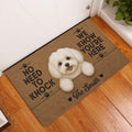 Maltese dog doormat displayed at a home entryway on a warm wood floor beside a white door
