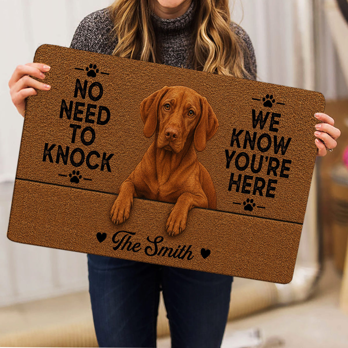 Person holding a brown Vizsla dog doormat with paw prints and bold lettering