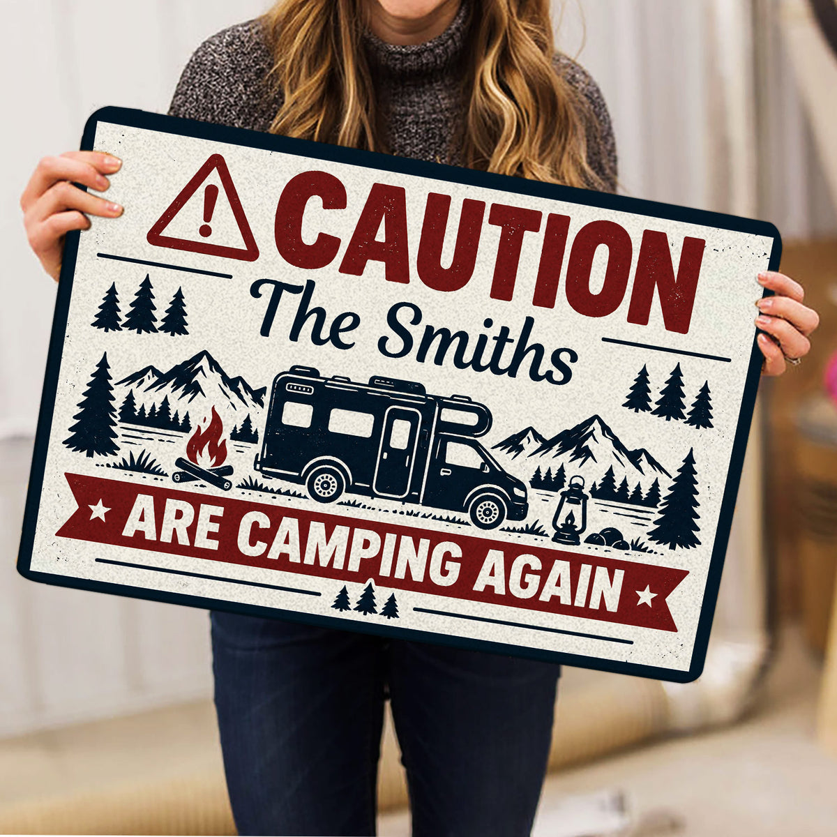 Person holding a vintage camping doormat featuring an RV, mountains, trees and campfire illustration