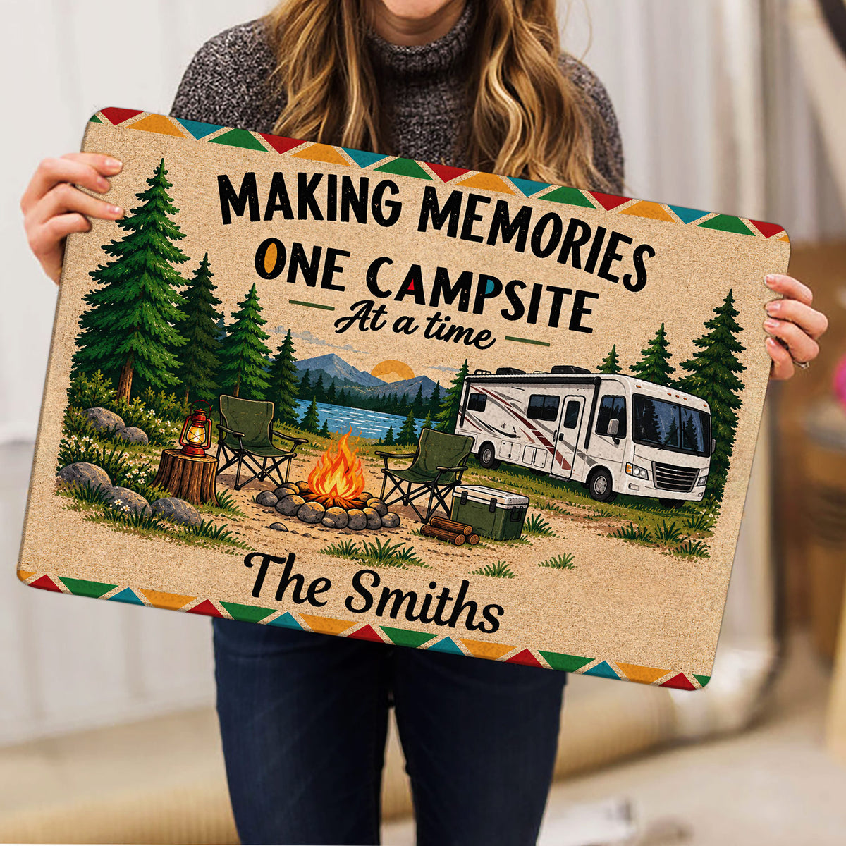 Camping rug held indoors, showing a colorful RV campsite scene with campfire, lake, trees, and chairs