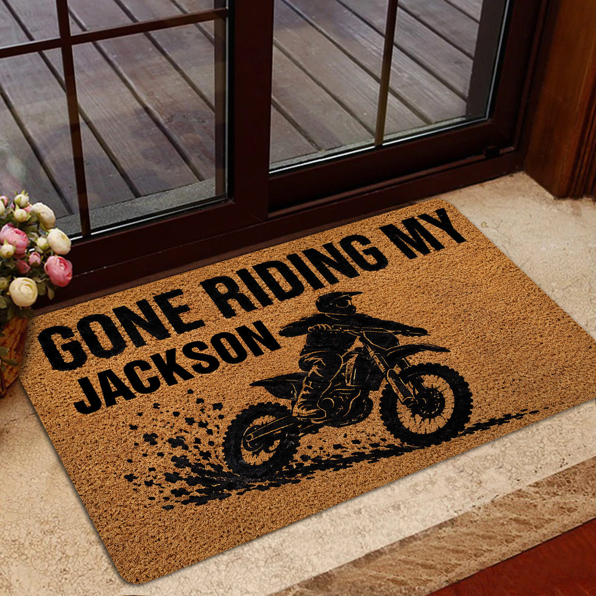 Motocross entryway mat with dirt bike rider artwork positioned beside a glass door