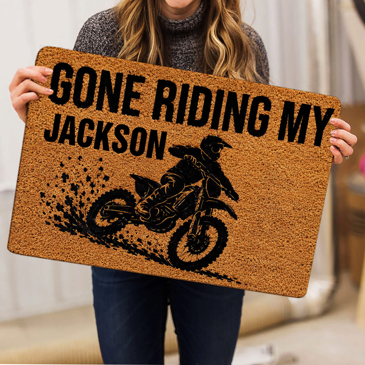 Motocross doormat held indoors, featuring a black dirt bike rider silhouette and muddy trail