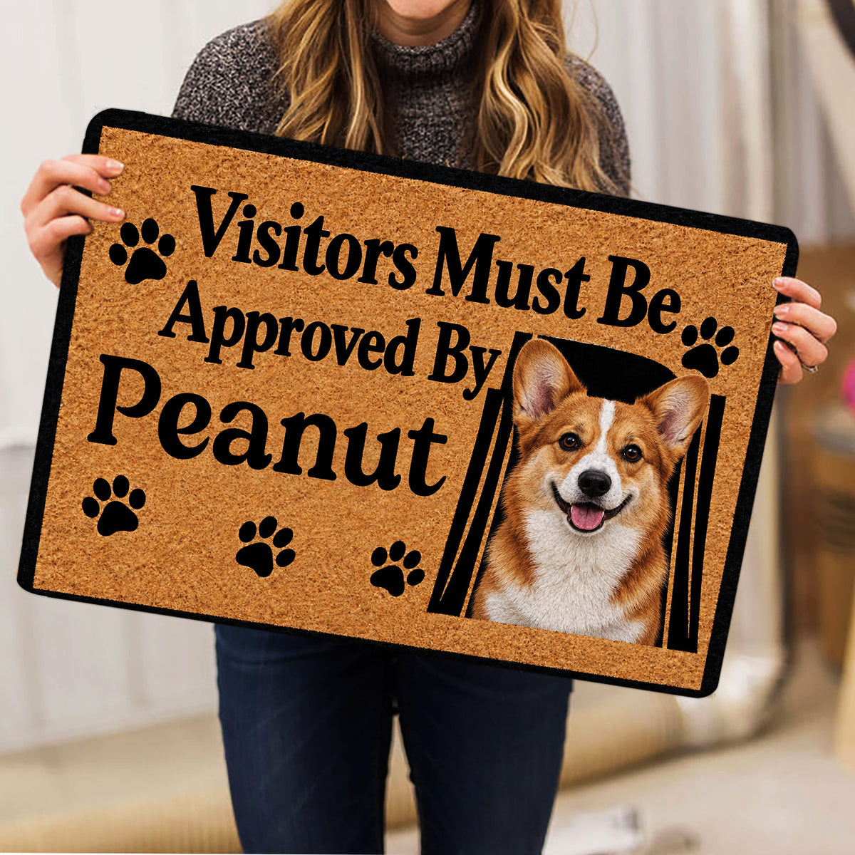 Corgi doormat held indoors, displaying a smiling corgi portrait, paw prints and bold black lettering
