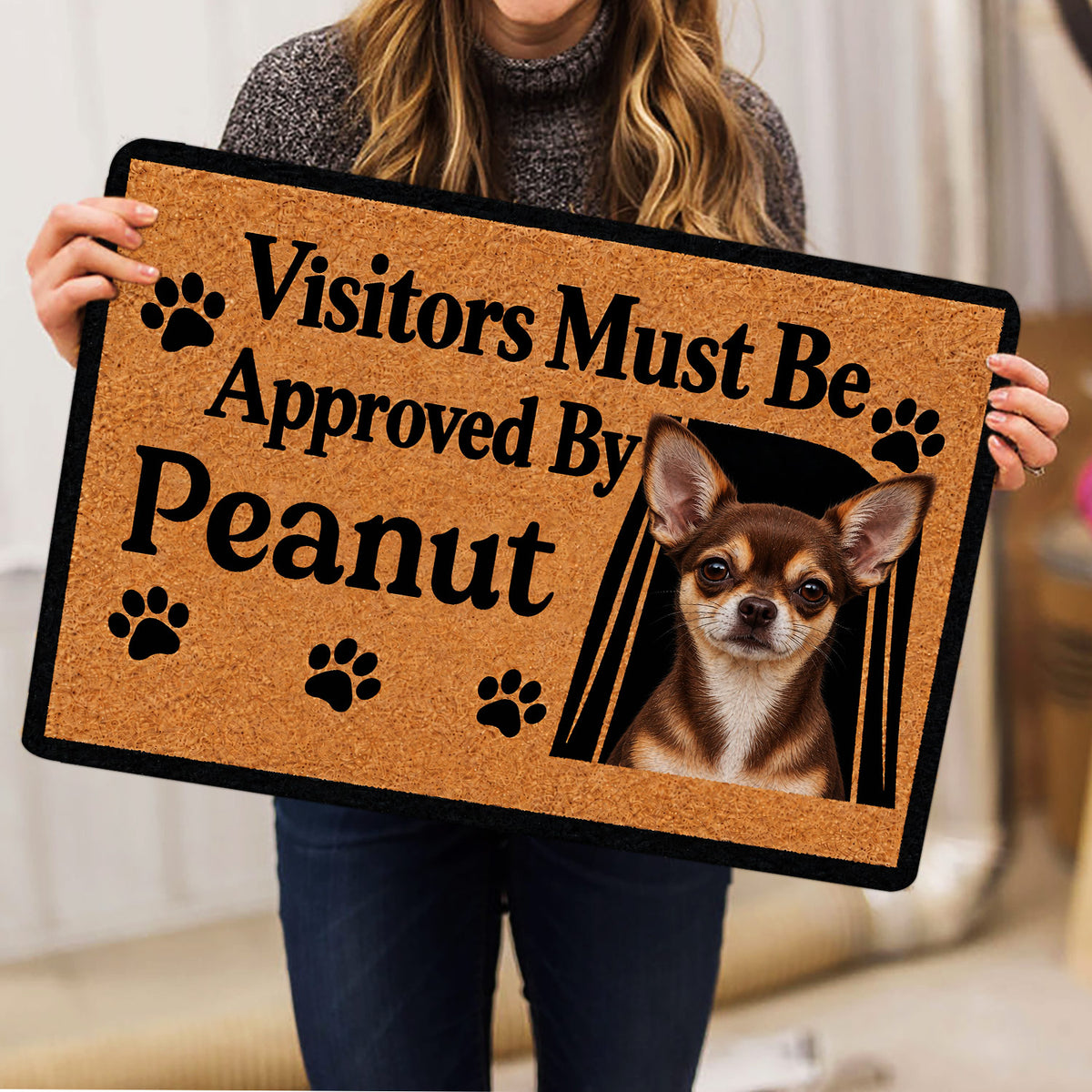 Person holding a Chihuahua doormat featuring paw prints and a framed dog portrait