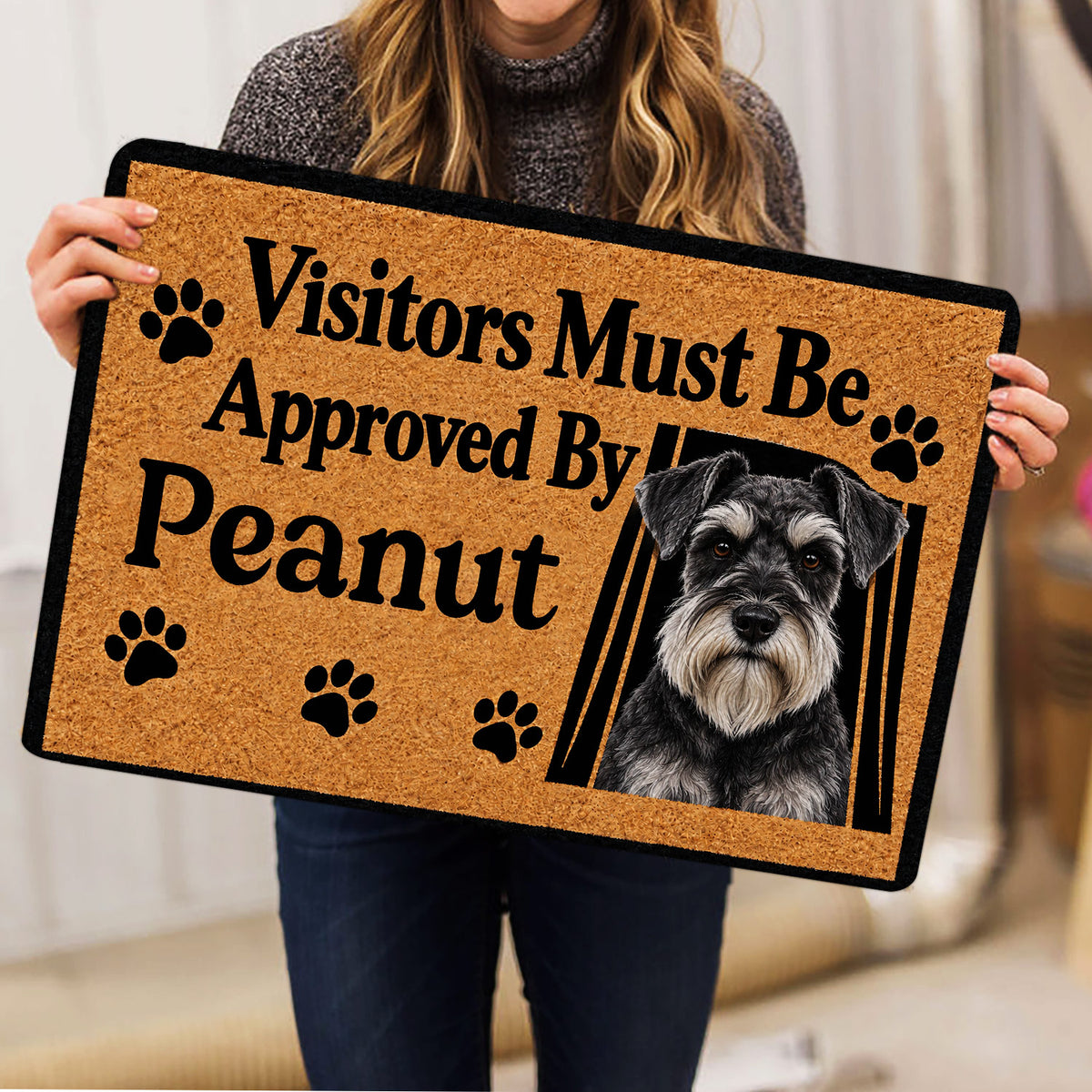 Person holding a Miniature Schnauzer doormat featuring a portrait, paw prints, and bold black lettering
