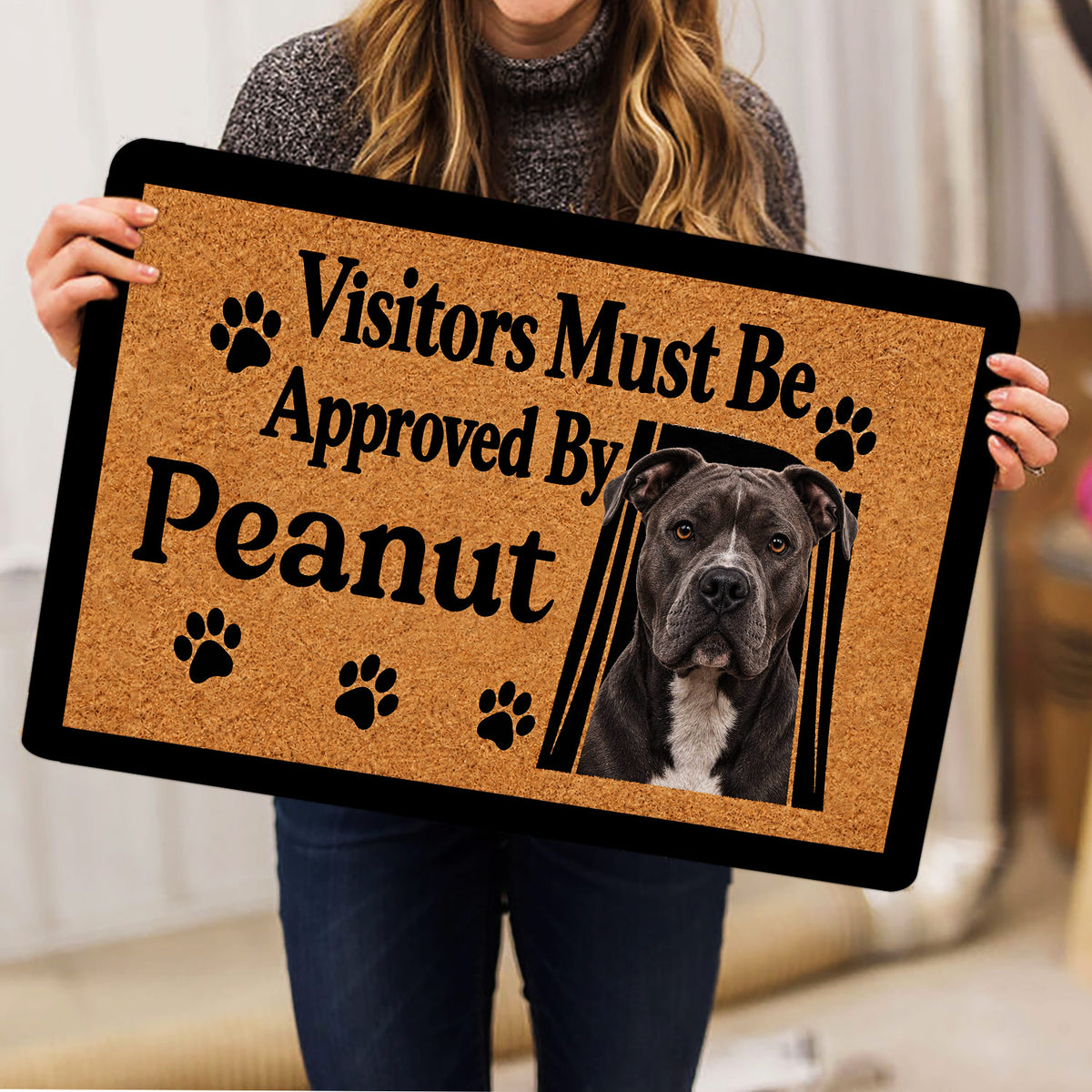 Person holding a pitbull doormat with bold visitor approval lettering, paw prints, and a realistic dog portrait