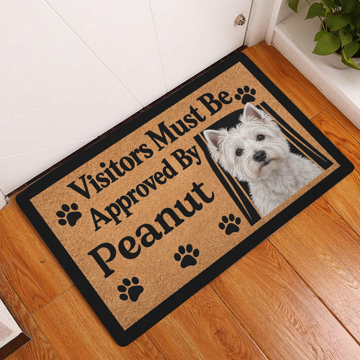 Westie doormat styled in an indoor entryway beside a white door and wooden flooring