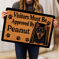 Person holding a Miniature Pinscher doormat featuring a black and tan dog portrait and paw prints