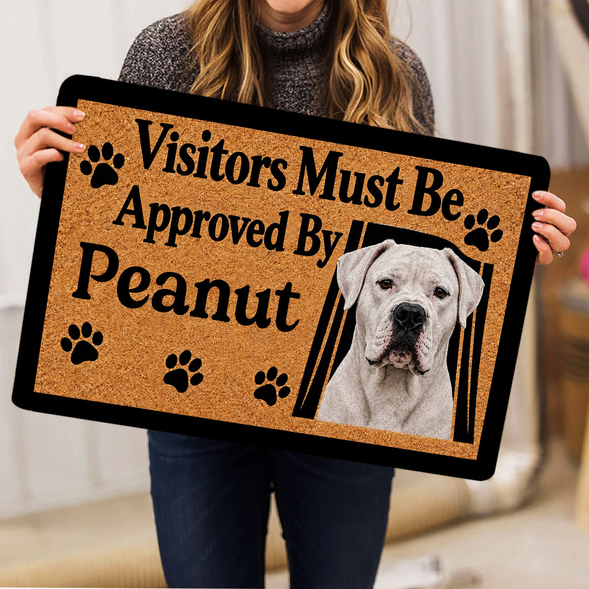 Person holding a Dogo Argentino doormat featuring a white dog portrait and black paw prints