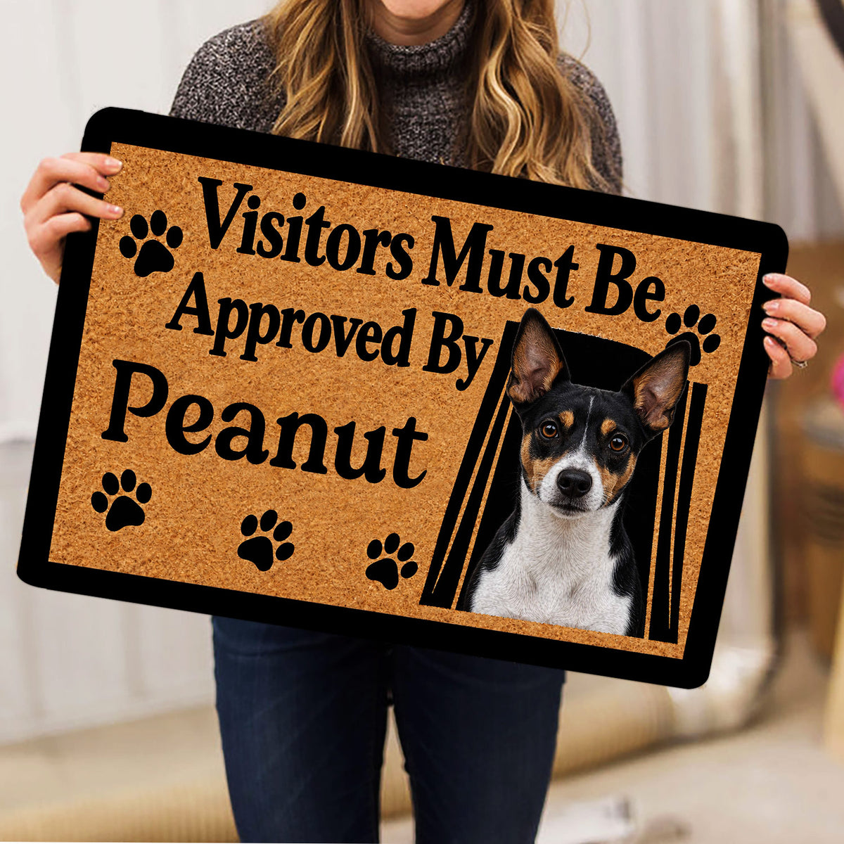 Person holding a Rat Terrier doormat with a dog portrait, paw prints, and bold black lettering