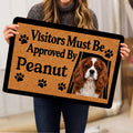 Person holding a Cavalier King Charles Spaniel doormat with a playful visitor message and paw prints