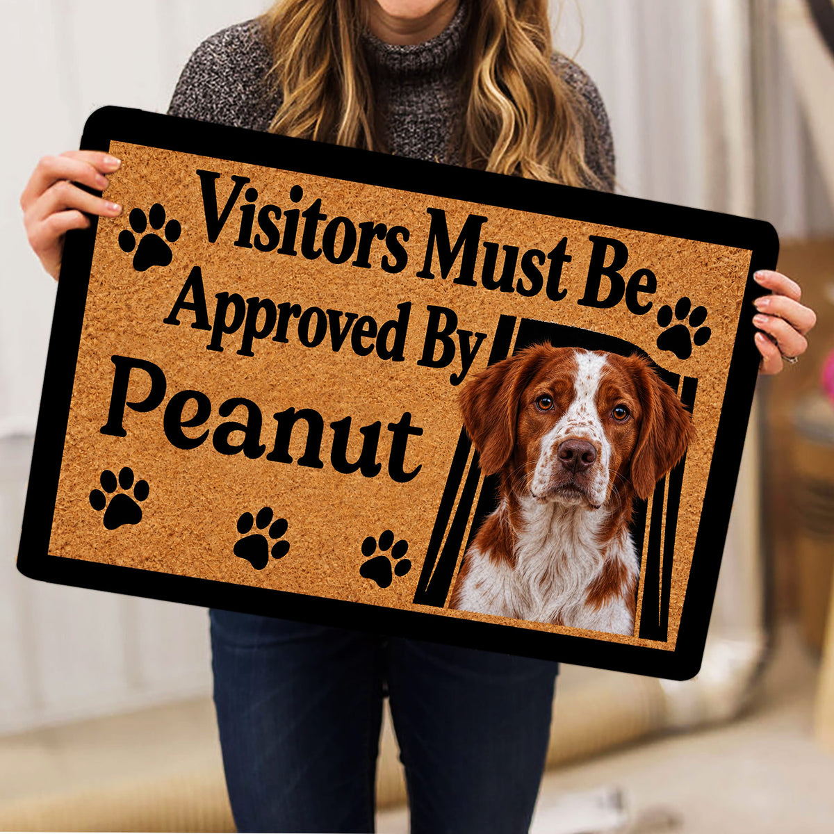 Person holding a Brittany Spaniel doormat featuring a dog portrait, paw prints, and tan artwork