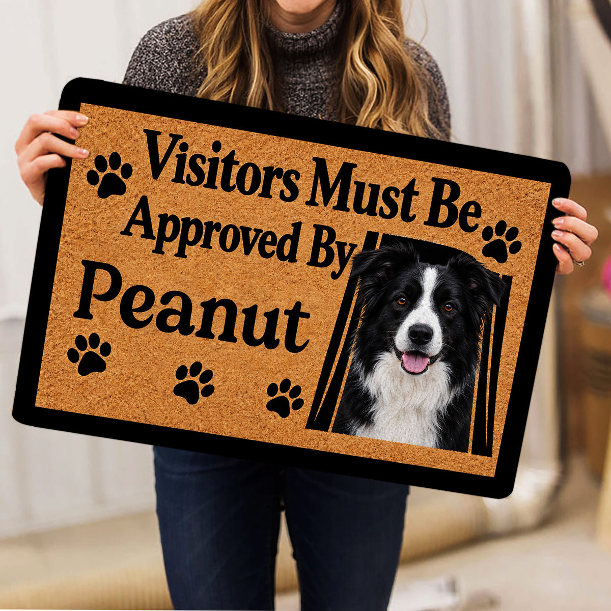 Person holding a Border Collie doormat featuring a smiling black-and-white dog and paw prints