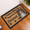 Sheltie dog doormat displayed at an indoor entryway beside a white door and wood flooring