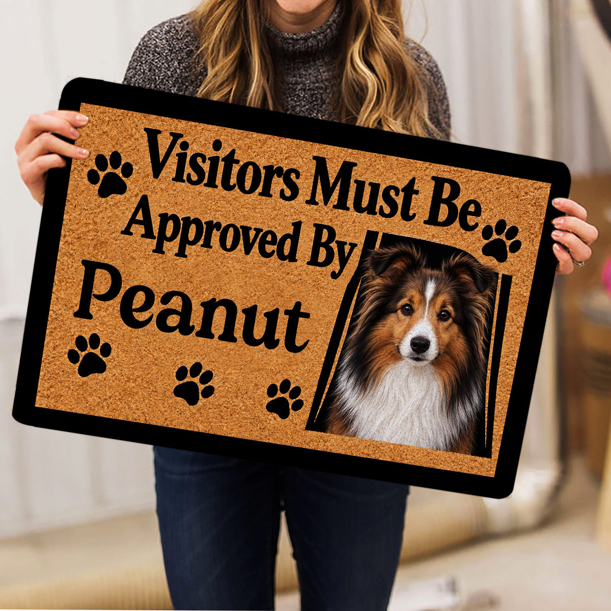 Person holding a Sheltie portrait doormat with paw-print artwork in a home setting