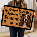 Person holding a Basset Hound doormat featuring paw prints and a friendly visitor message
