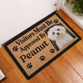 Maltese dog doormat styled by a white entry door on a wood floor in a home entryway