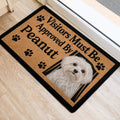 Maltese dog entryway mat beside a doorway, showing the tan artwork, paw prints, and black border