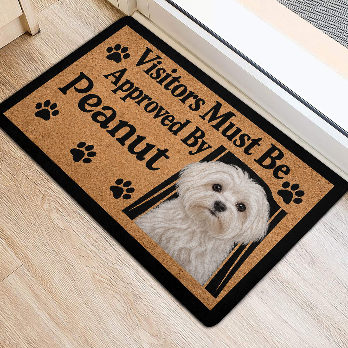Maltese dog entryway mat beside a doorway, showing the tan artwork, paw prints, and black border