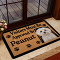 Maltese dog doormat displayed at a glass doorway with a warm tan design and paw print accents