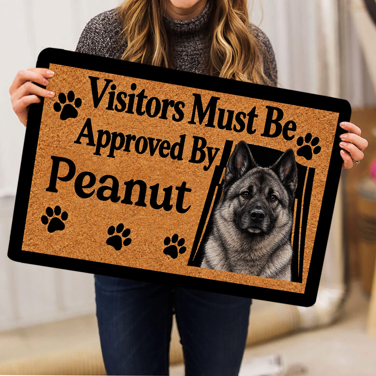 Person holding a Norwegian Elkhound doormat featuring a gray dog portrait, paw prints, and visitor lettering