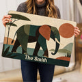 Person holding an elephant doormat displaying abstract foliage, geometric shapes, and an earthy landscape palette