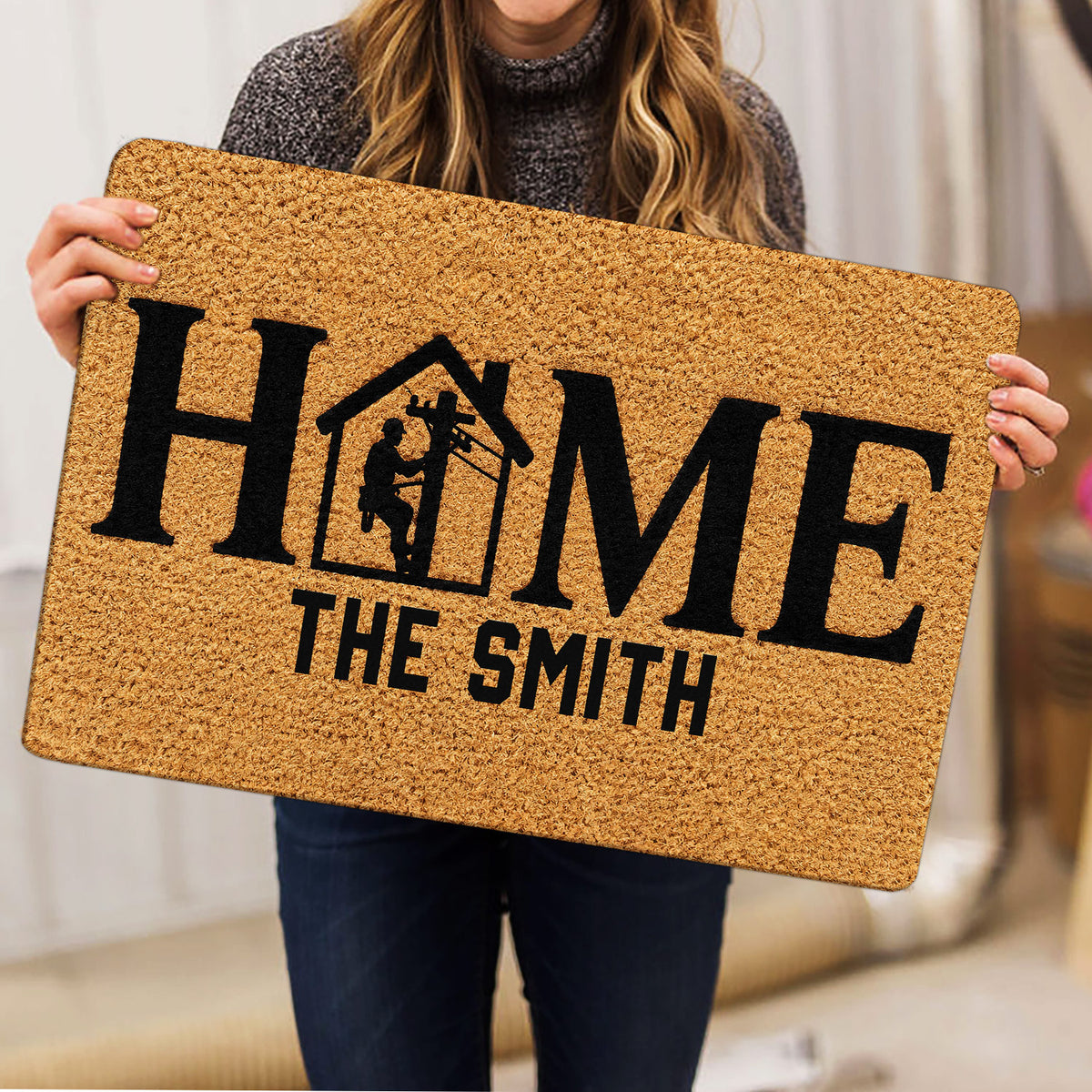 Lineman-themed HOME doormat held indoors, showing the tan surface and bold black artwork