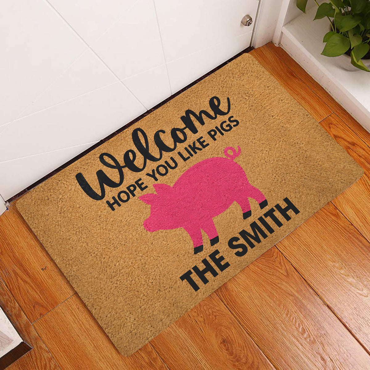 Pig-themed welcome doormat displayed by a white entry door over a warm wood floor