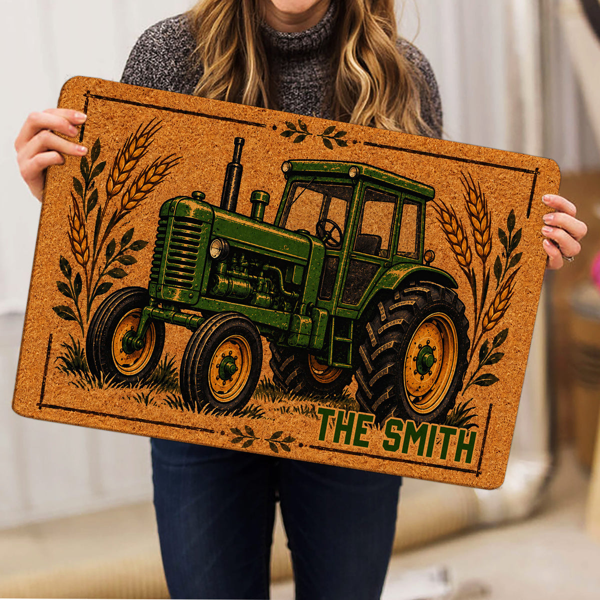Person holding a tractor doormat featuring vintage farm artwork, wheat stalks, and earthy colors