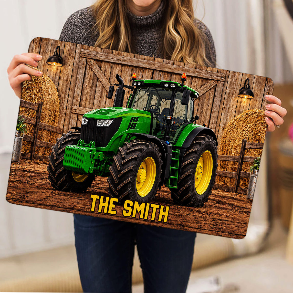 Person holding a tractor doormat featuring a barn scene, hay bales, and bold lettering
