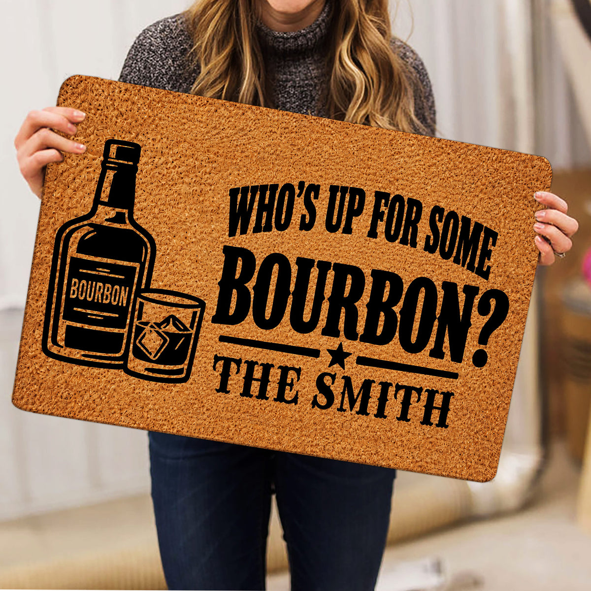 Person holding a bourbon doormat featuring a bottle, whiskey glass, and bold black typography