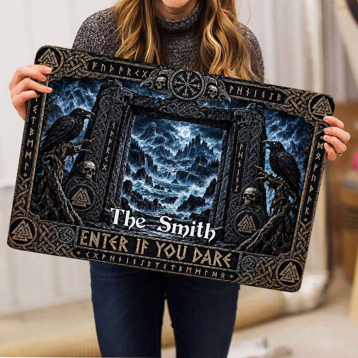 Person holding a Viking doormat featuring ravens, skulls, knotwork, and a moonlit mountain landscape