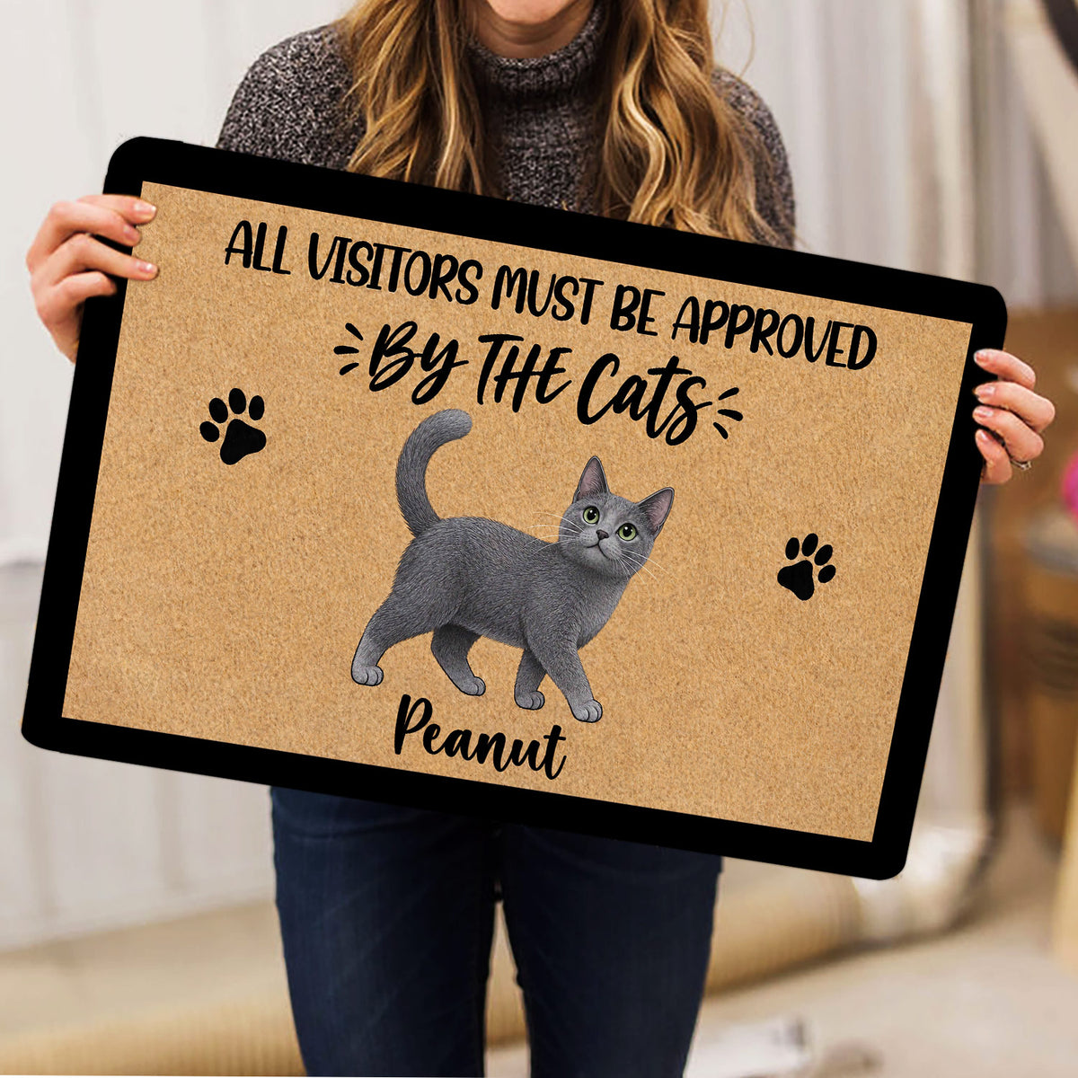 Person holding a gray cat doormat featuring paw prints and playful entryway artwork