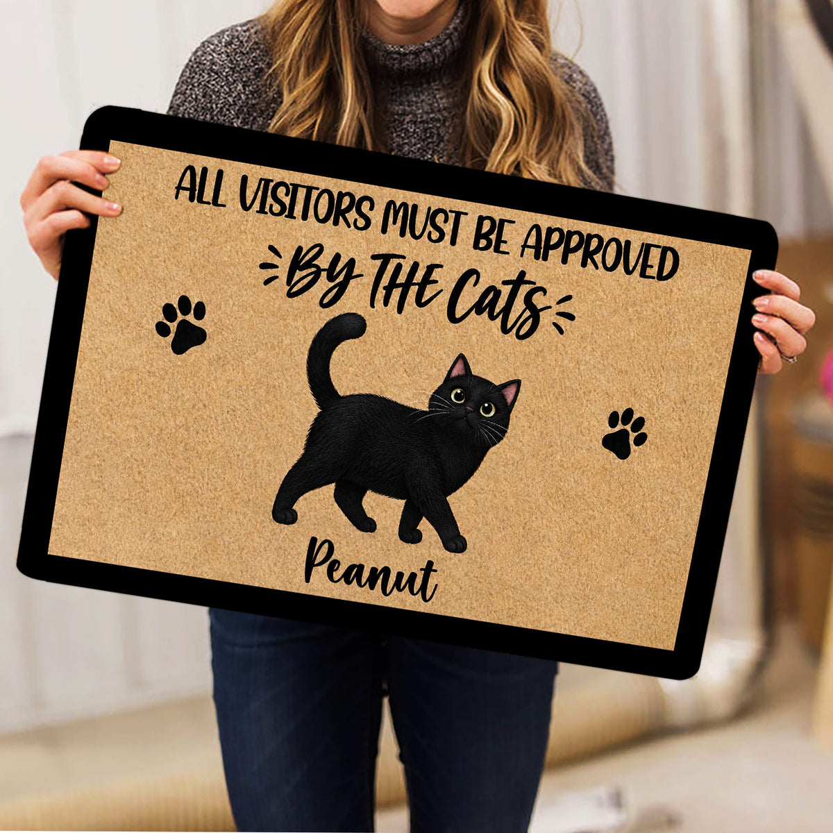 Person holding a black cat doormat featuring paw prints and a playful cat-themed design
