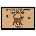 Custom Burmese cat doormat featuring a brown cat illustration, black paw prints, the quote All Visitors Must Be Approved By The Cats, custom pet name, tan textured background and black border.