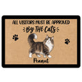 Rectangular cat doormat with a fluffy brown and white long-haired cat, black paw prints, and a playful visitors-approved-by-cats quote on a tan coir-look background with a black border.