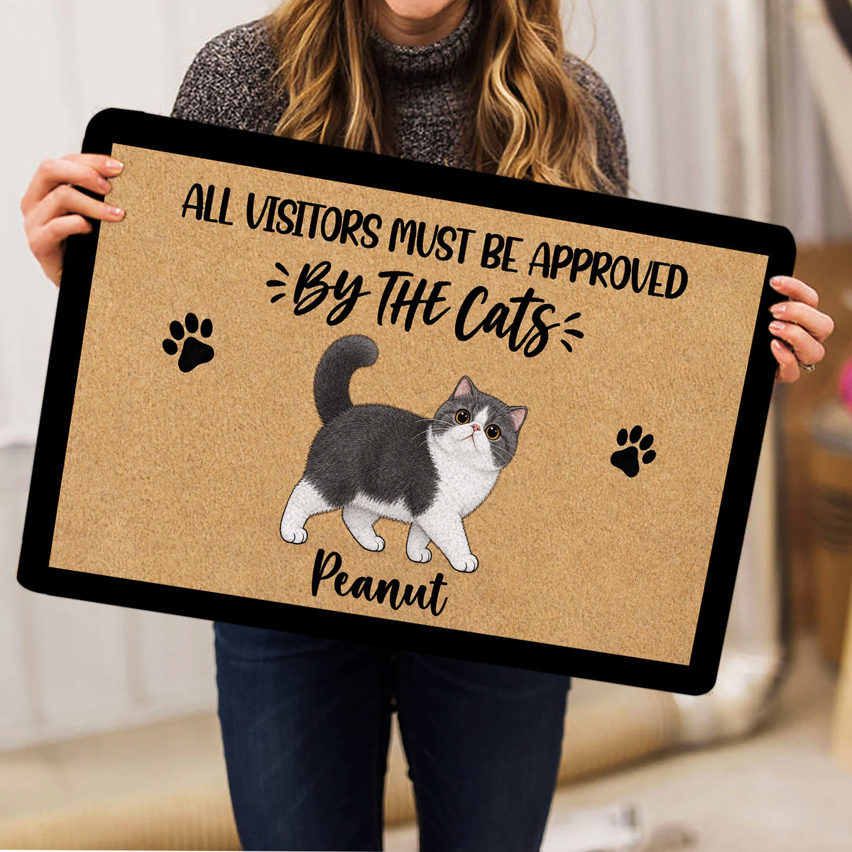 Person holding a cat-themed doormat featuring an Exotic Shorthair illustration