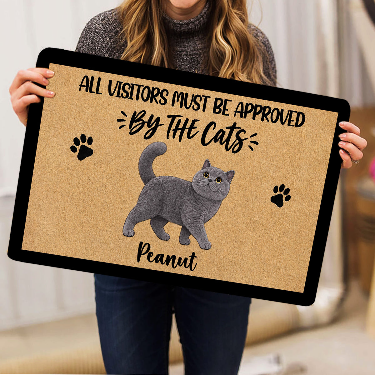Person holding a British Shorthair cat doormat featuring paw prints and cat artwork