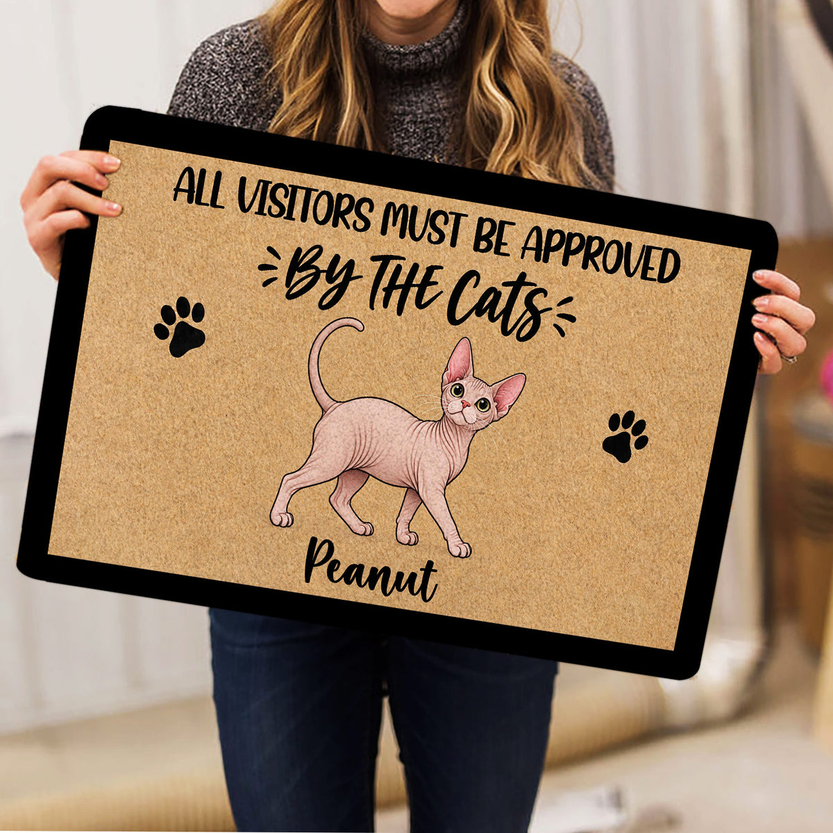 Person holding a Sphynx cat doormat featuring paw prints and a playful illustrated cat design