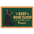 Black cat doormat with paw prints and playful door-closed escape message on a green background