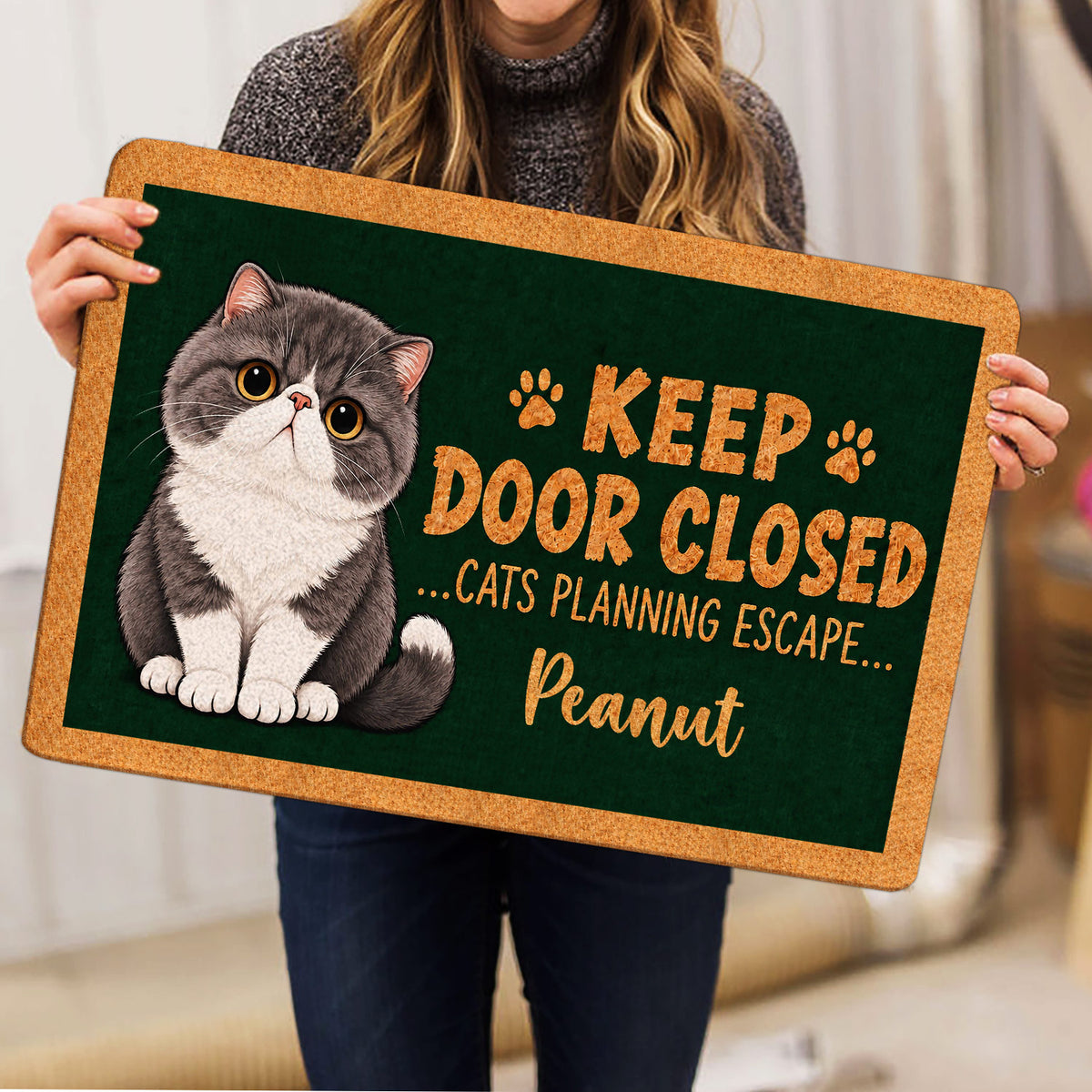 Person holding an Exotic Shorthair cat doormat featuring paw prints and playful entryway artwork