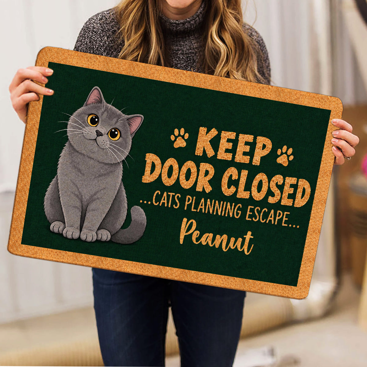 British Shorthair cat doormat held indoors, showing the full green artwork and tan border