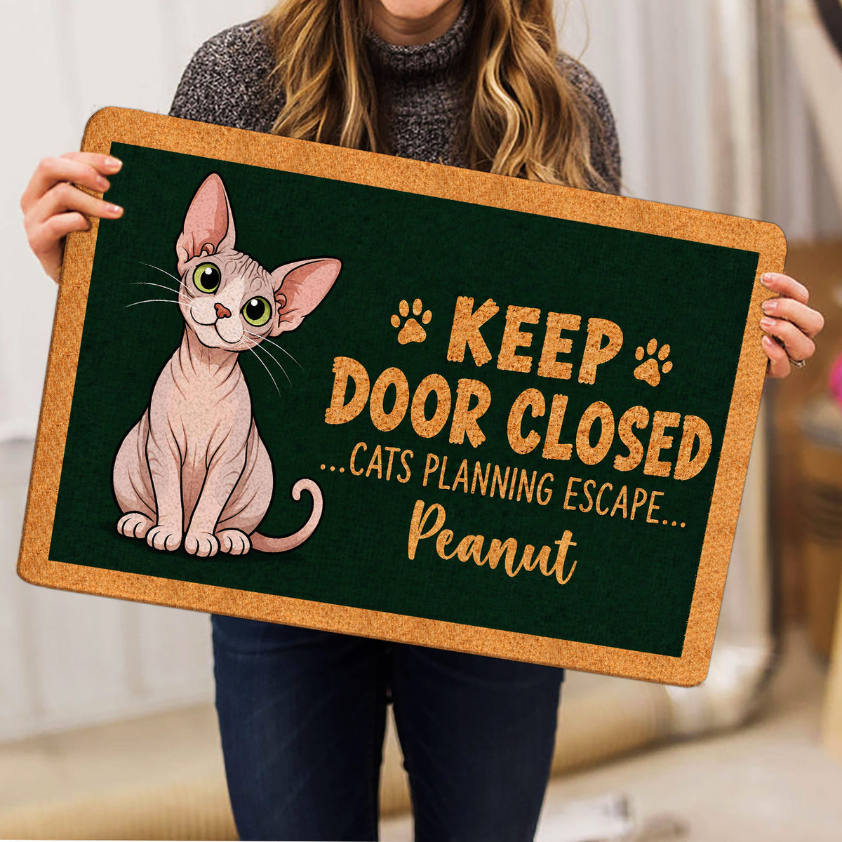 Person holding a Sphynx cat doormat featuring playful paw prints and escape-themed artwork