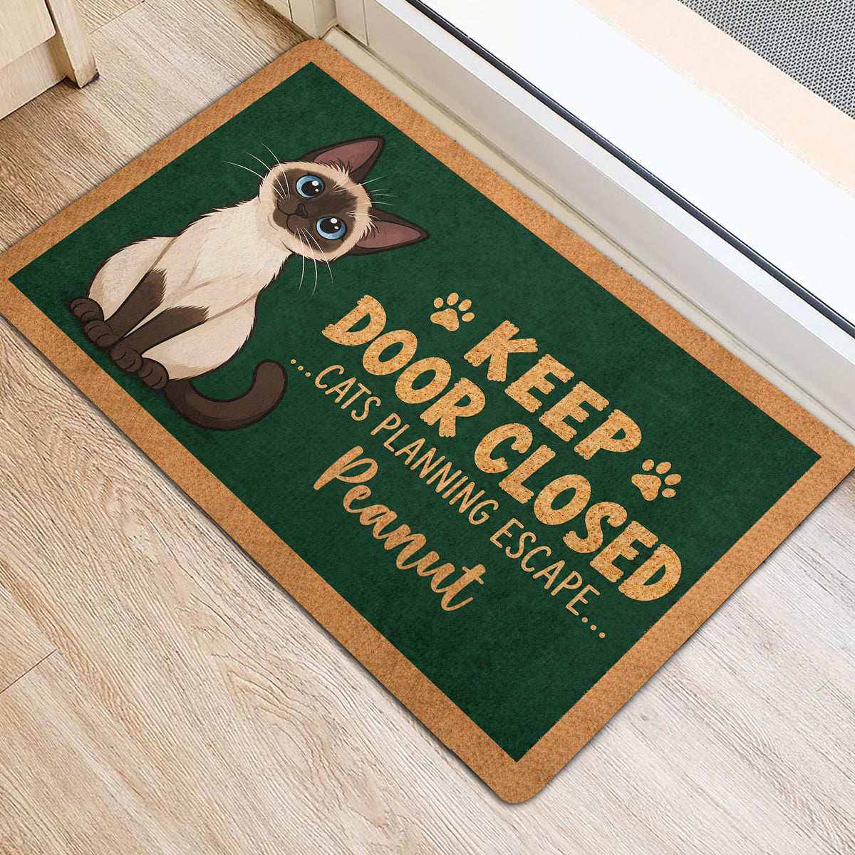 Siamese cat door mat shown near a bright doorway with green artwork and tan border