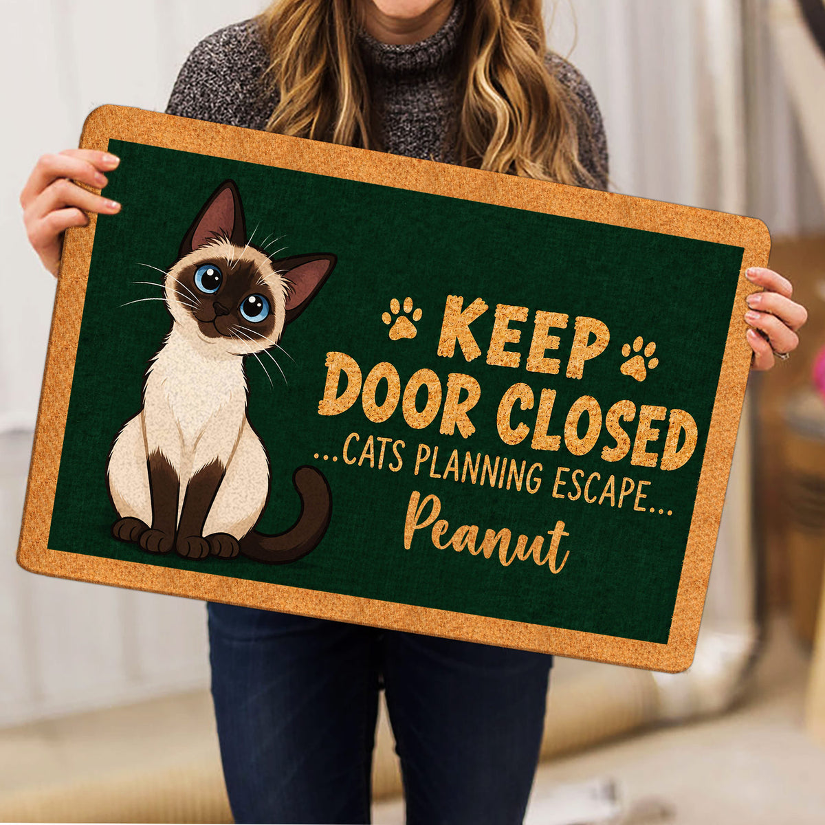 Siamese cat doormat held indoors, showing the illustrated cat, paw accents, and green artwork