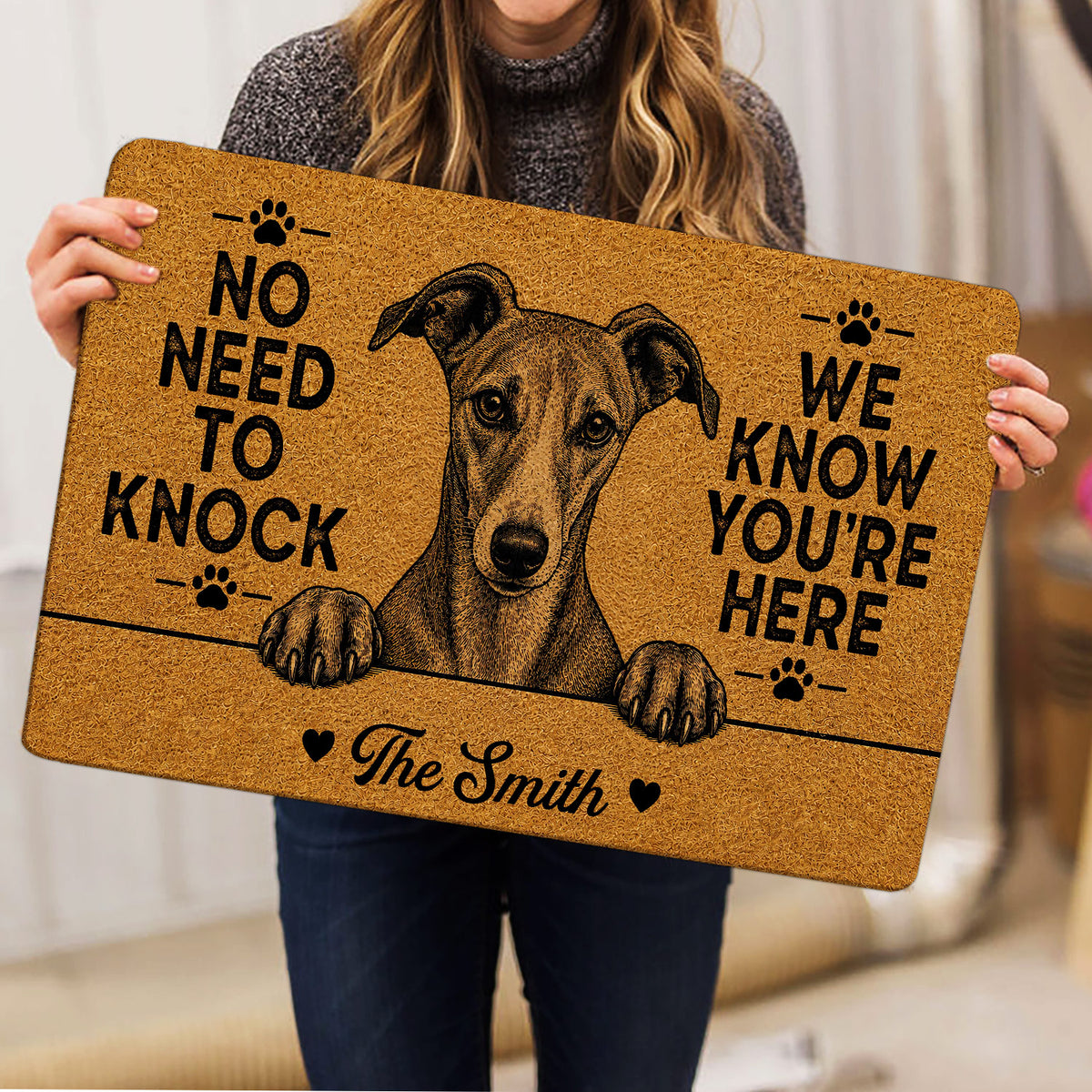 Person holding a tan Whippet doormat featuring a detailed dog portrait, paw prints, hearts, and bold lettering