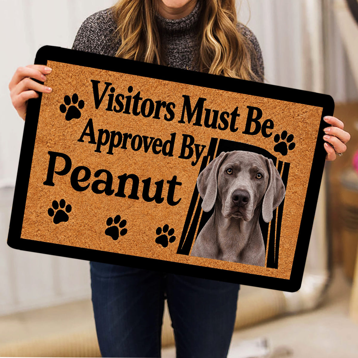 Person holding a Weimaraner doormat featuring a gray dog portrait, paw prints, and bold lettering