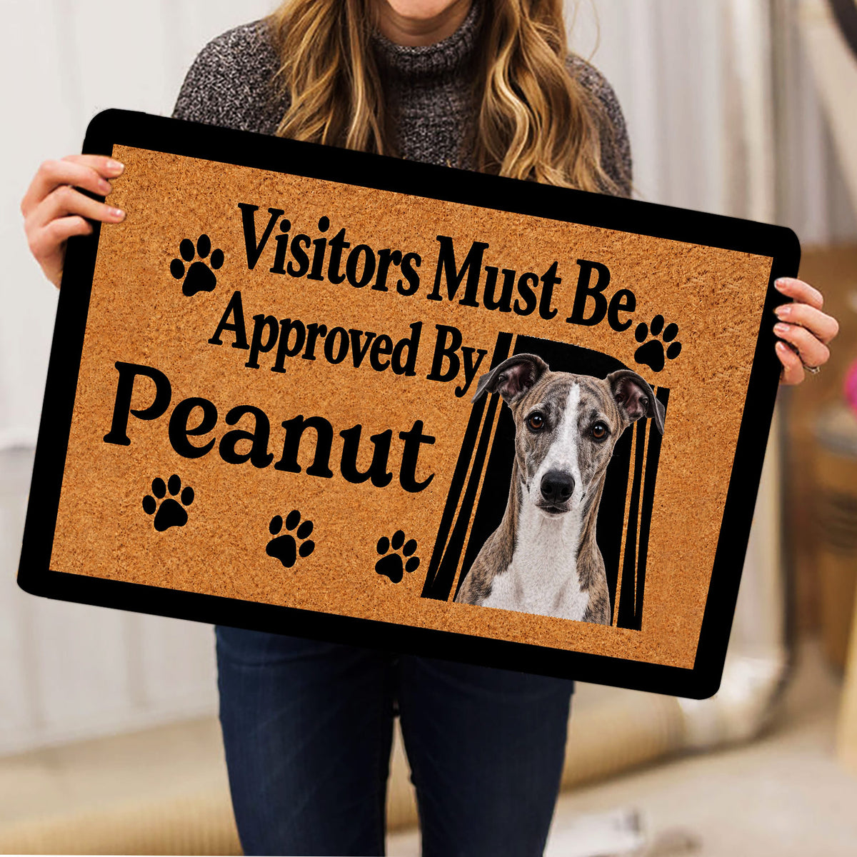 Person holding a Whippet doormat featuring a dog portrait, paw prints, and playful typography