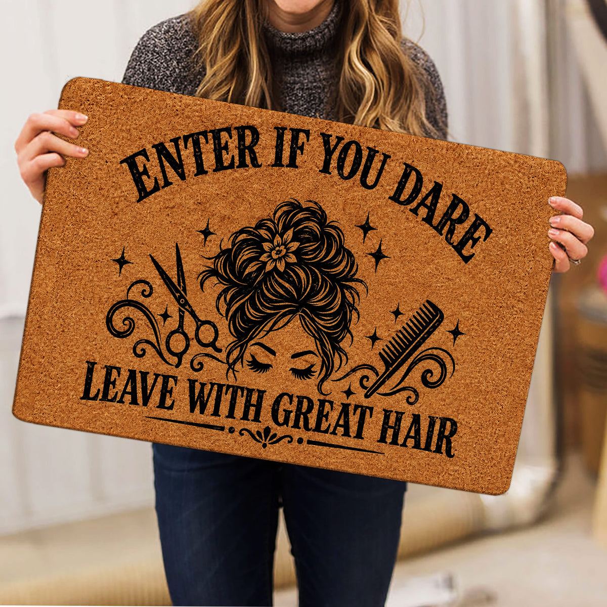 Person holding a hairstylist doormat featuring a woman’s hairstyle, scissors, comb and bold black artwork
