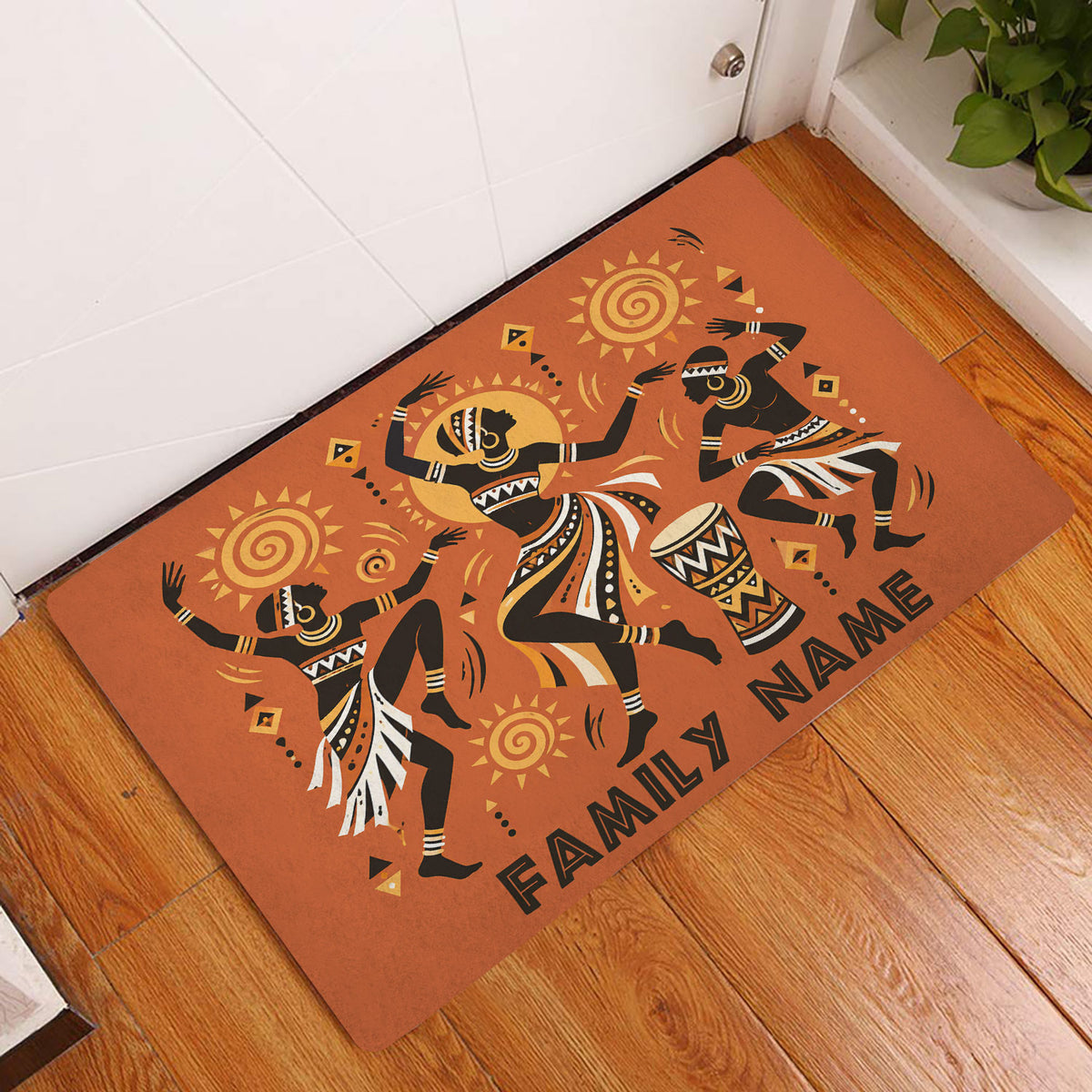 African dance doormat displayed in an indoor entryway on a wood floor beside a white door